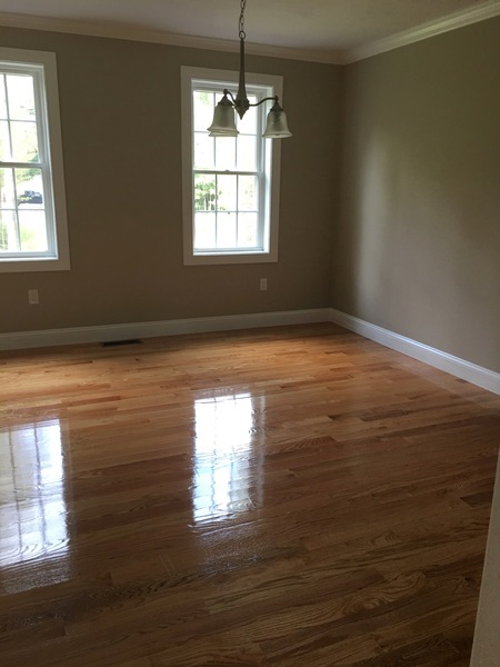 Empty room with polished hardwood floors, beige walls, and two windows letting in sunlight.