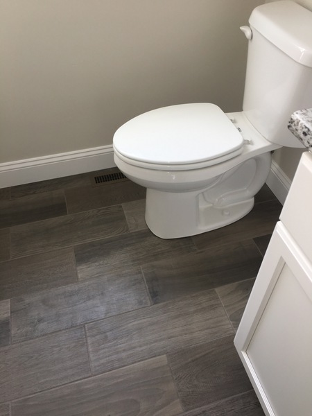 White toilet on gray wood-look tile floor next to a white vanity in a bathroom.