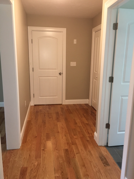 Hallway with light wood floors, beige walls, and three white doors, one slightly open.