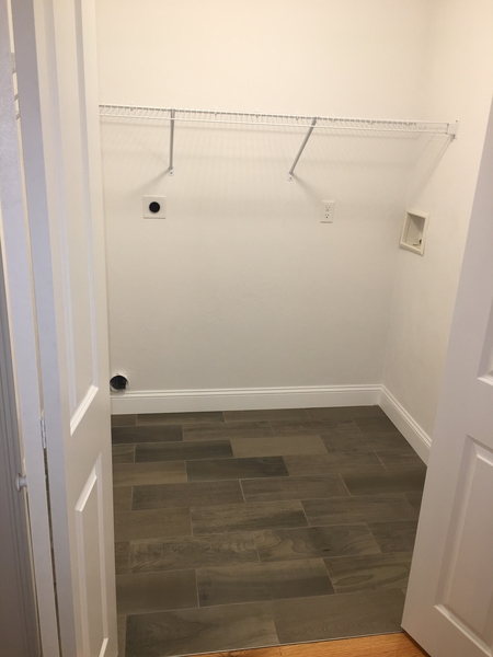 Empty laundry room with tiled floor, white walls, and a wire shelf on the back wall.