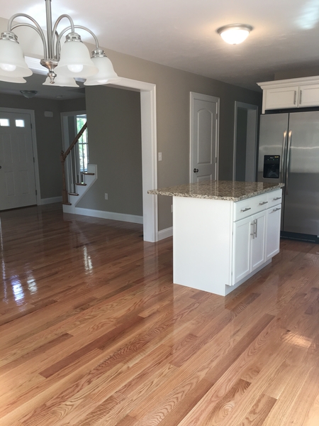 Modern kitchen with granite island, stainless fridge, and shiny hardwood floors.