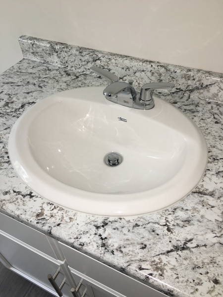 White oval sink with chrome faucet set in a speckled granite countertop.
