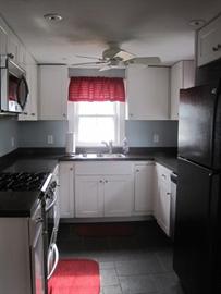 Small kitchen with white cabinets, black appliances, and a red curtain over the window.