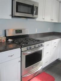 Modern kitchen with stainless steel stove and microwave, white cabinets, and red rug.