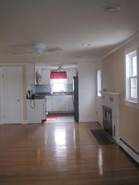 Bright living room with hardwood floors, fireplace, and view into a small kitchen area.