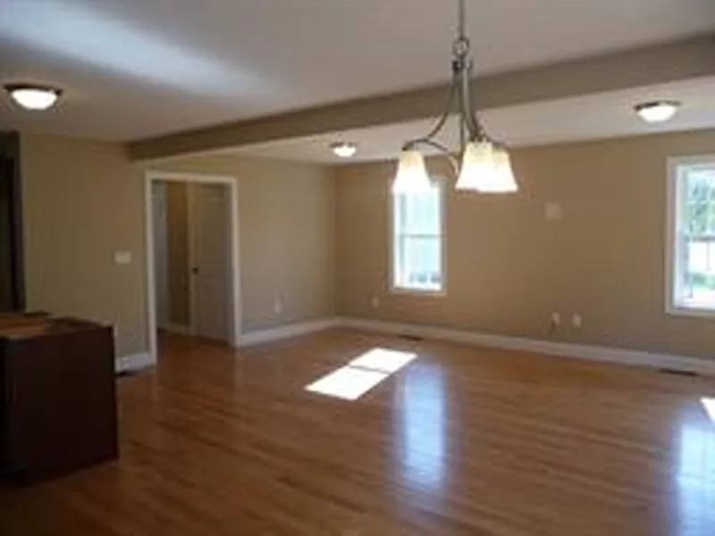 Spacious empty room with hardwood floors, beige walls, and ceiling lights.