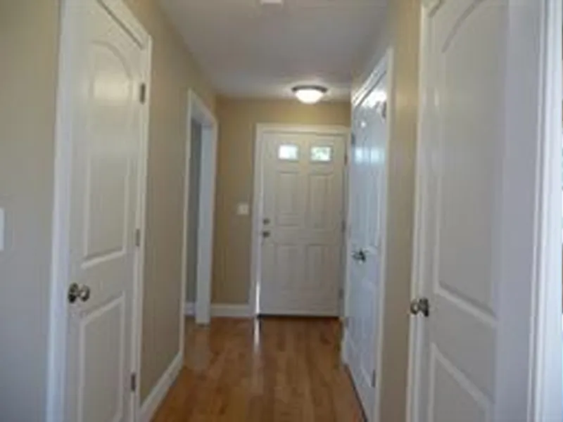 A hallway with wooden floor, beige walls, and white doors leading to a front door.
