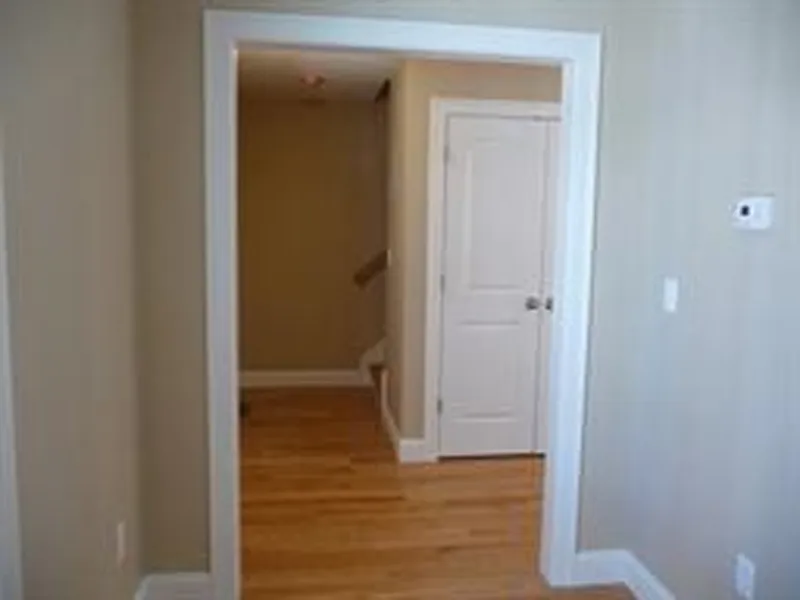 View of a doorway leading to a small hallway with a closed white door and wooden floor.