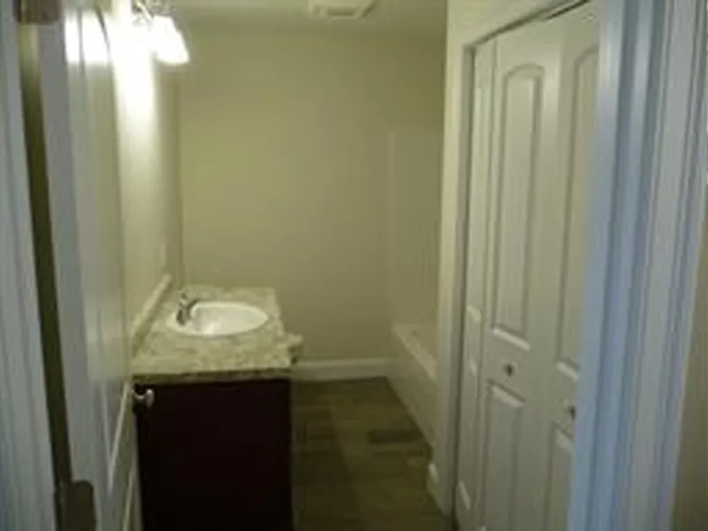 Narrow bathroom with a sink, granite countertop, closet doors, and bathtub in the back.