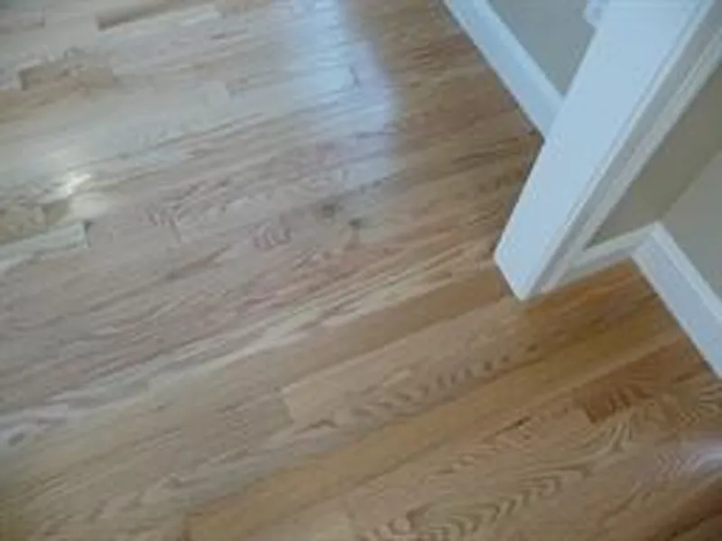 Light-colored hardwood floor with natural grain, beside white trim and a wall corner.