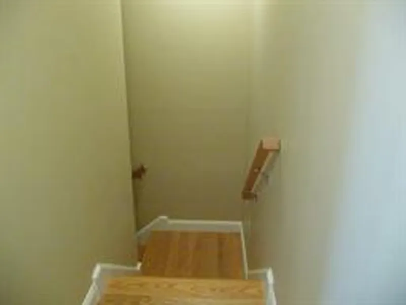 Wooden staircase with beige walls and a simple handrail on the right side.