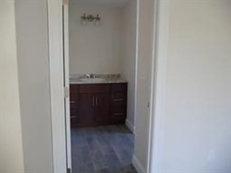 Open doorway leading to a bathroom with a dark wood vanity and light-colored walls.