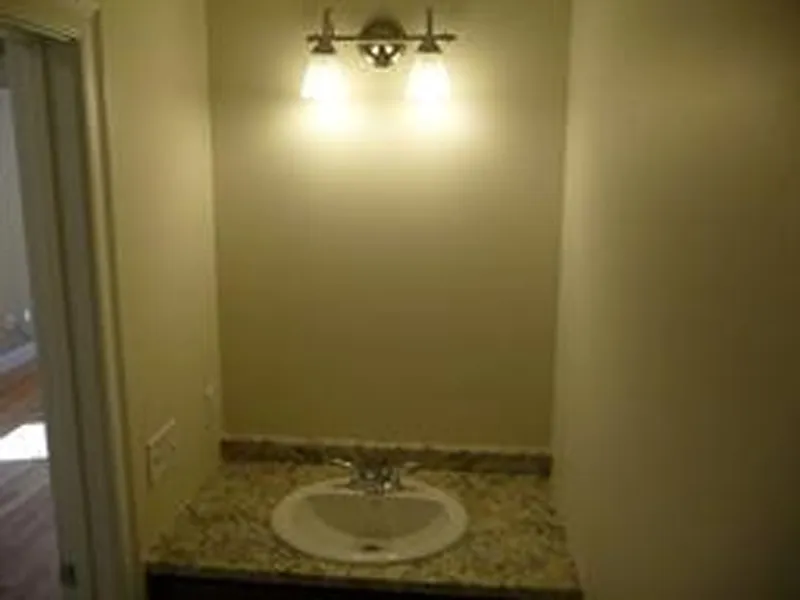 Small bathroom vanity with granite countertop, sink, and wall-mounted light fixture above.