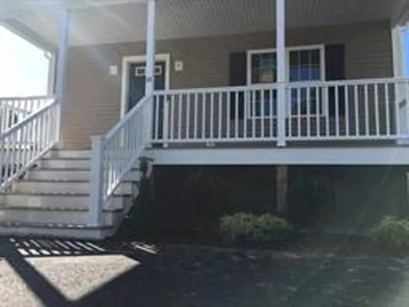 Front steps and porch of a tan house with white railings and a black door.