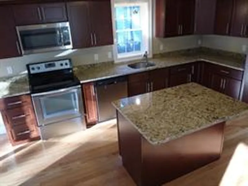 Modern kitchen with stainless appliances, dark cabinets, and a granite island countertop.
