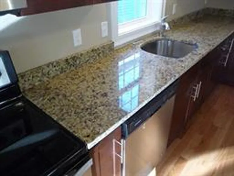 Granite kitchen countertop with sink, stove, dishwasher, and wooden cabinets.