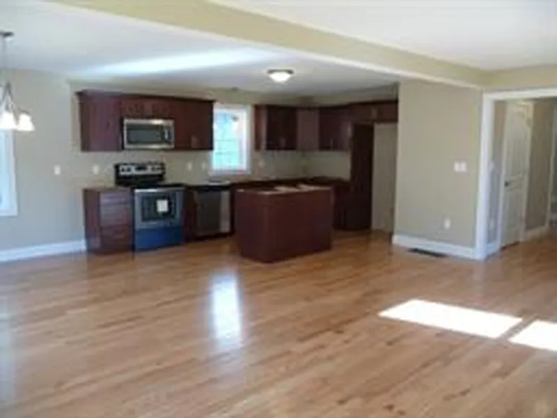 Open kitchen with dark cabinets, stainless appliances, and hardwood floors in bright room.