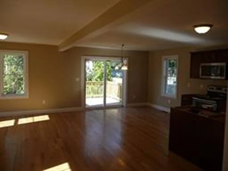 Spacious room with wood floors, large windows, kitchen area, and sliding glass door.