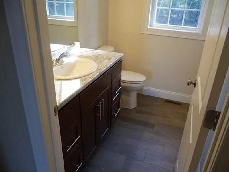 Small bathroom with a marble countertop, sink, toilet, mirror, and window.