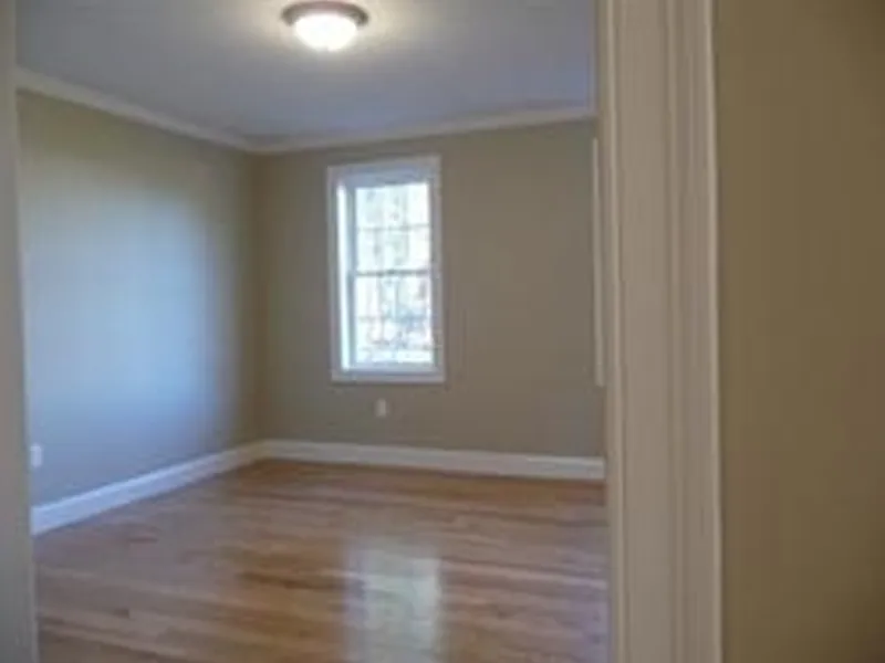 Empty room with tan walls, hardwood floors, and a window letting in natural light.