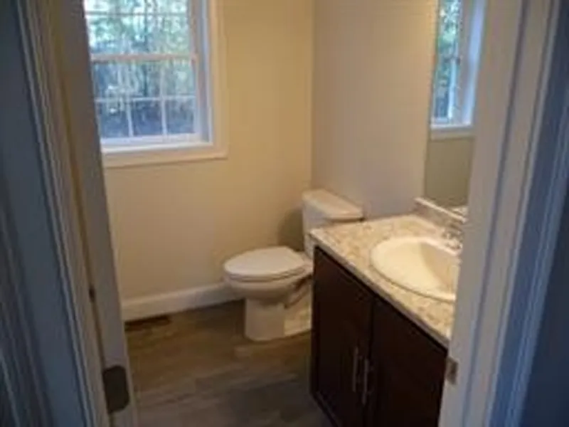 Small bathroom with a toilet, sink, cabinet, and two windows with natural light.