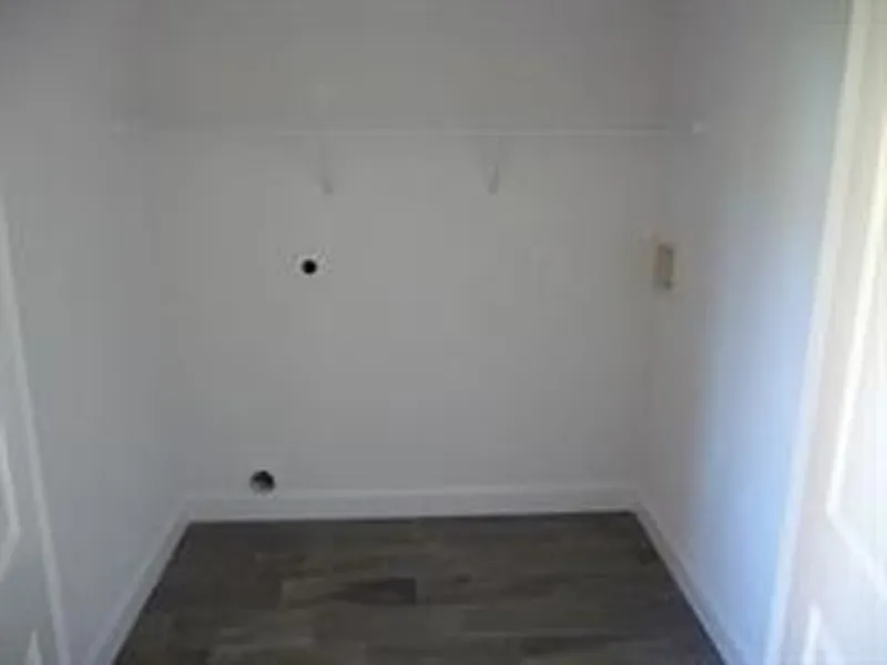 Empty white closet or laundry area with two small wall holes and a shelf bracket.