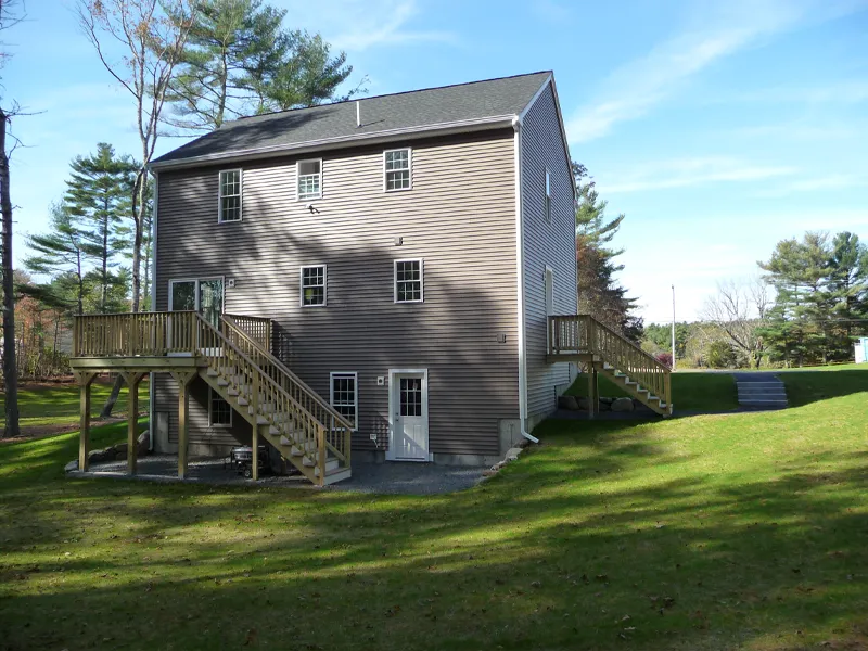 Three-story house with beige siding, two wooden staircases, and a grassy yard with trees.