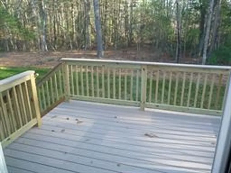 A small wooden deck with railing overlooks a grassy yard and forested area.