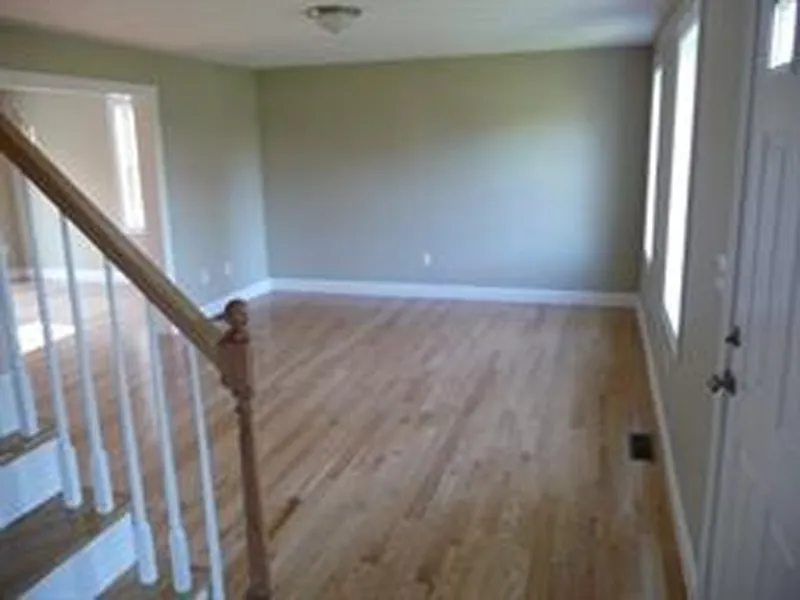 Empty living room with hardwood floors, beige walls, and a staircase with white rails.