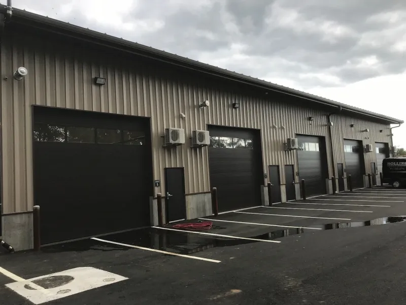 Large industrial building with five closed garage doors and empty parking spaces outside.