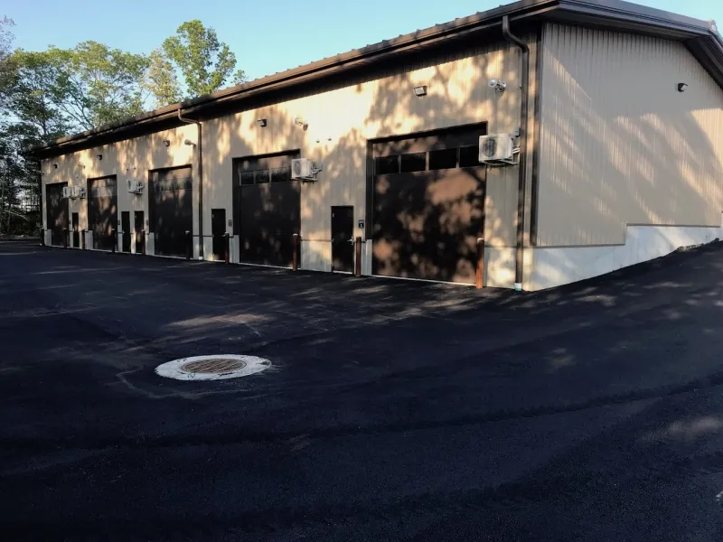 Tan industrial building with multiple large garage doors and newly paved asphalt lot.