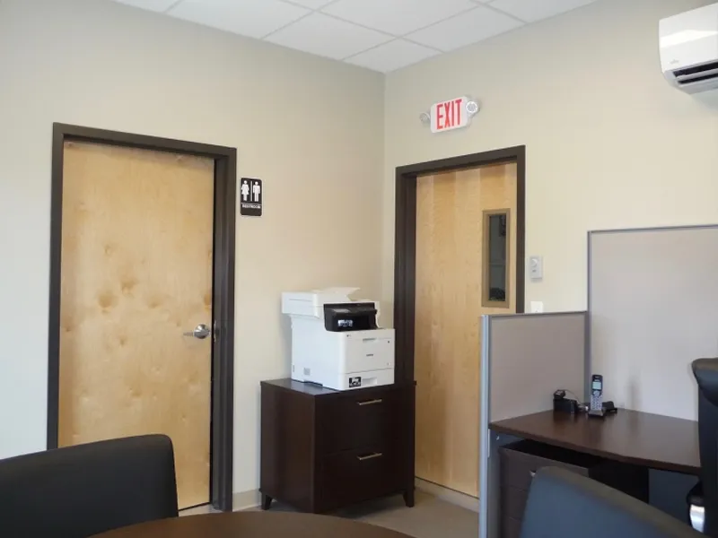 Office interior with a printer, wooden doors, and a table with chairs in the foreground.