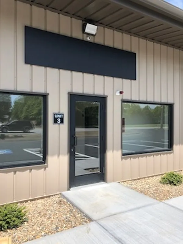Glass door entrance to Unit 3 of a tan commercial building with empty window spaces.