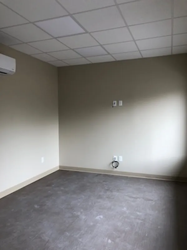 Empty room with beige walls, gray floor, and a white ceiling with fluorescent lights.