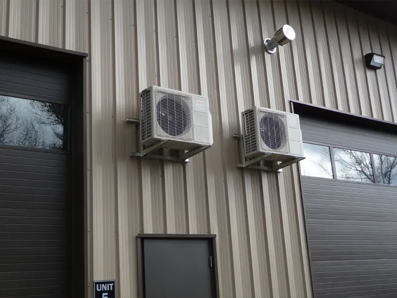 Two air conditioning units mounted on the exterior wall of a metal building.