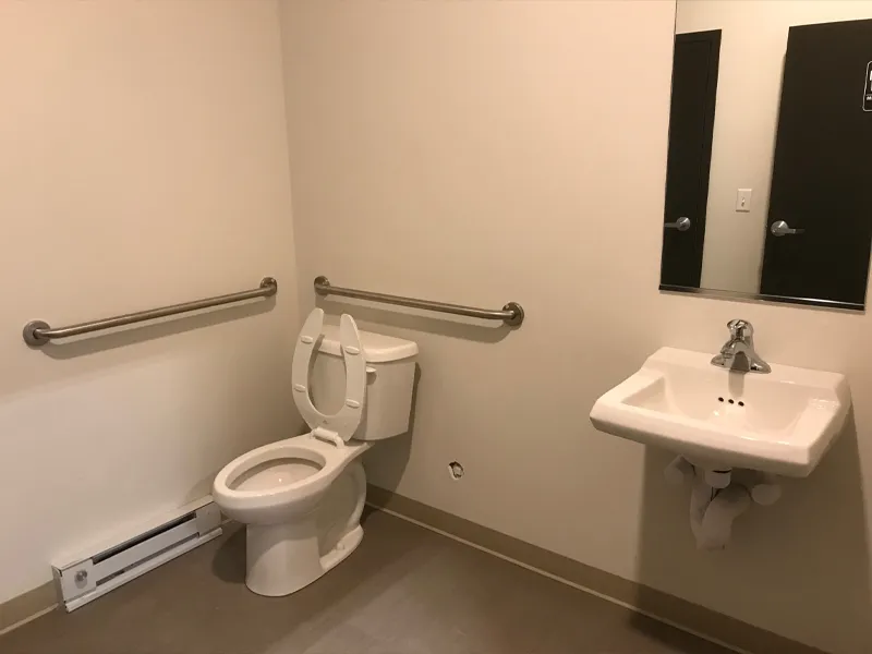 An accessible restroom with grab bars, a toilet, and a sink with a mirror above it.