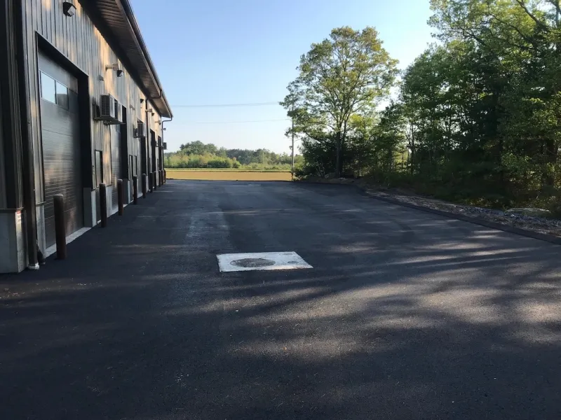 Freshly paved blacktop beside a building, with trees and grass in the background.