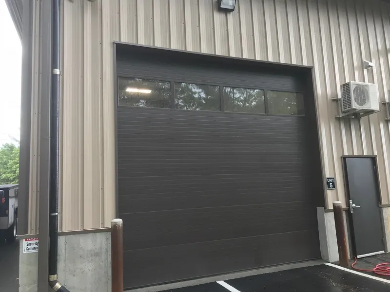 A large dark garage door with windows on a beige industrial building.