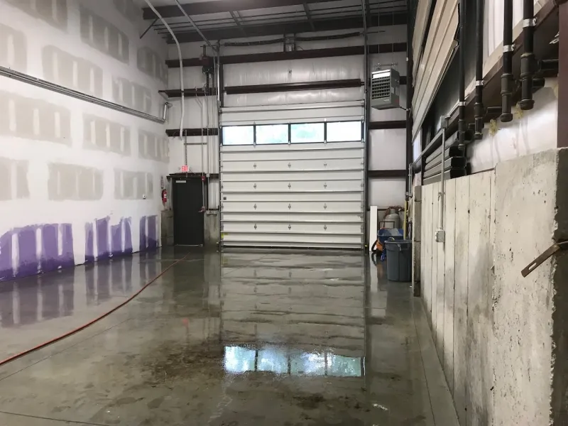 Interior of an empty warehouse with a closed garage door and polished concrete floor.