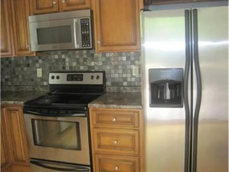 Stainless steel kitchen appliances with wood cabinets and a tiled backsplash.