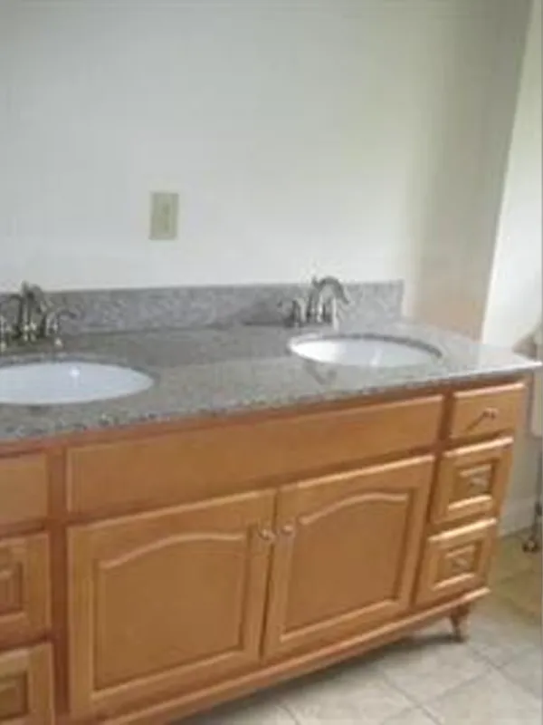 Double sink bathroom vanity with granite countertop and wooden cabinets underneath.