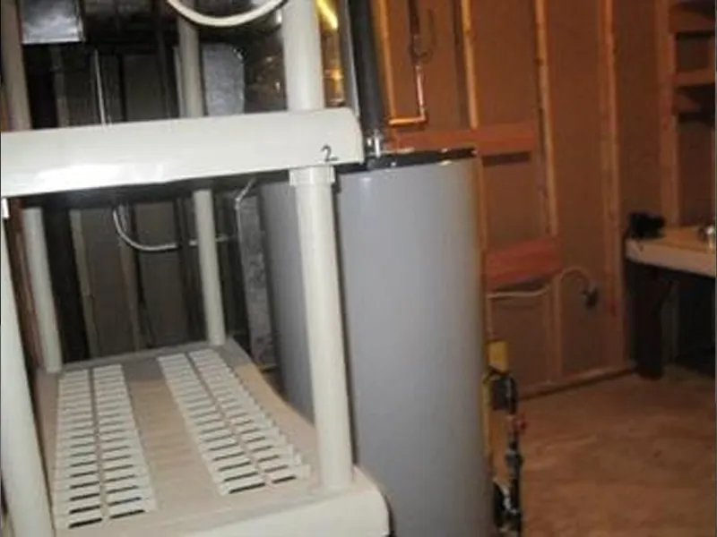 Gray water heater next to white utility shelf in an unfinished basement or utility room.