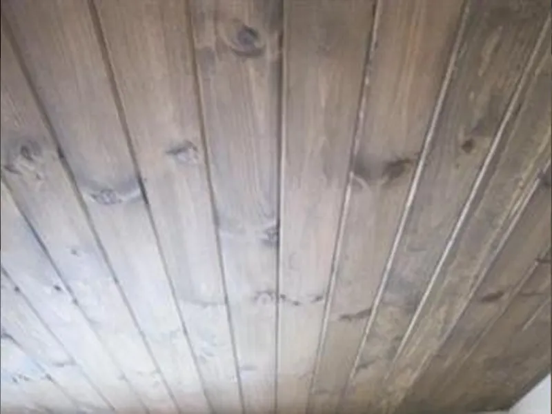 Wooden ceiling with visible knots and vertical planks in a natural brown finish.