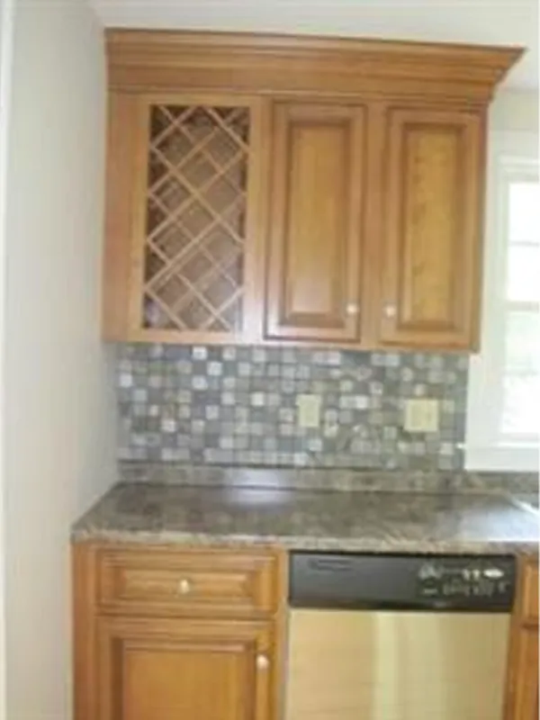 Wood kitchen cabinets with a wine rack, mosaic tile backsplash, and stainless dishwasher.