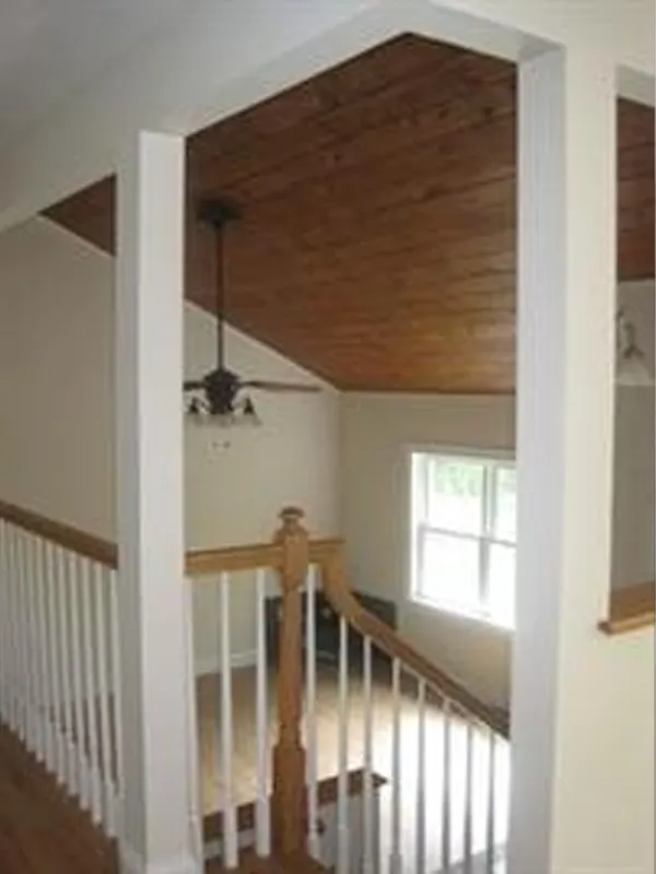 A ceiling fan installed just inches below a slanted wooden ceiling in a stairwell area.