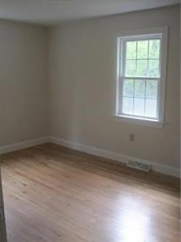 Empty room with beige walls, a window, and light wood flooring.