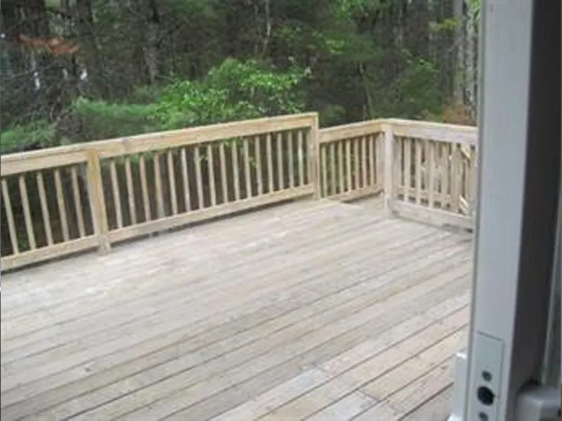 Wooden deck with simple railing overlooking trees, viewed from an open doorway.