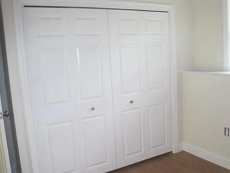 White double closet doors in a room with light-colored walls and wood flooring.