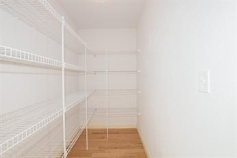 Empty walk-in pantry with white wire shelving and light wood flooring.