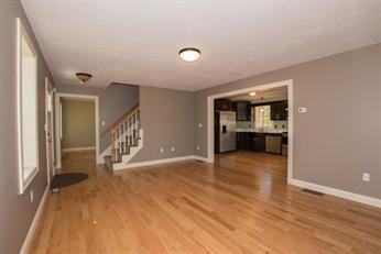 Spacious living area with hardwood floors, open to kitchen, and a staircase on the left.